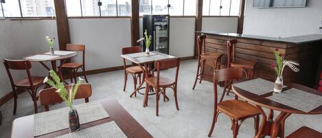A dining area with wooden tables and chairs, a refrigerator, and a TV mounted on the wall.