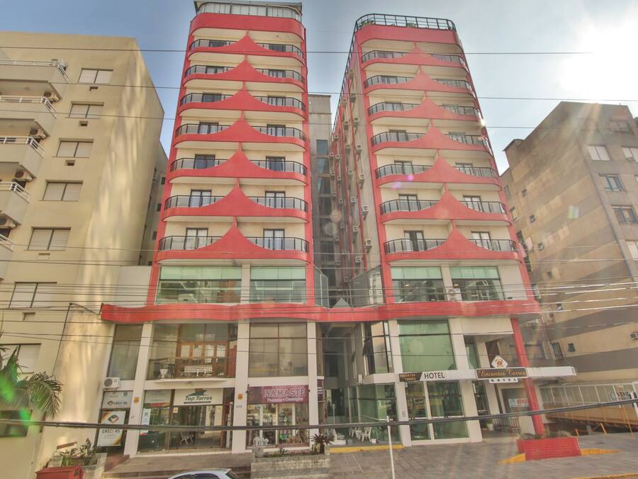 Un hotel de varios pisos con balcones, un restaurante a nivel de calle y un letrero visible del hotel llamado "Hotel Encantos".