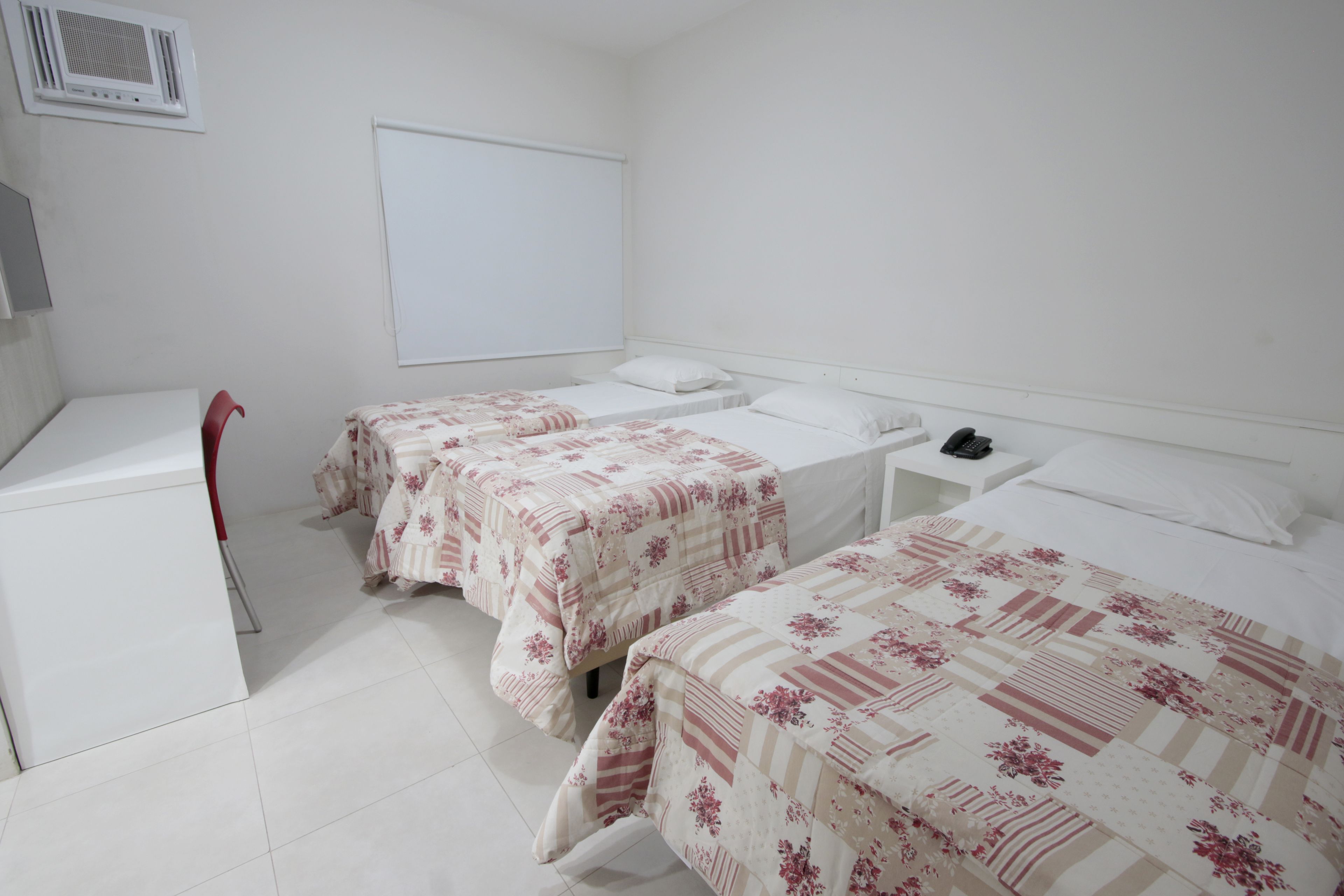 Una habitación limpia y minimalista con dos camas individuales, un escritorio y una silla.