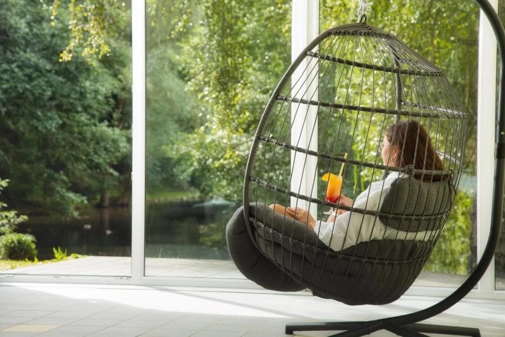 A person sitting in a hanging chair with a view of a lake and greenery.