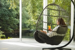 A person sitting in a hanging chair with a view of a lake and greenery. - Hotel zum Hirschen in Lam (Lam)