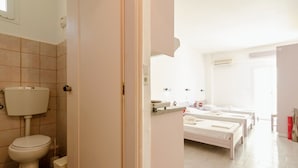 A bathroom with a toilet, sink, and two beds. - Village Oasis - Annex (Hersonissos)