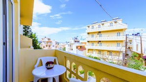 A balcony with a white table and chairs, overlooking a residential area with yellow buildings. - Village Oasis - Annex (Hersonissos)