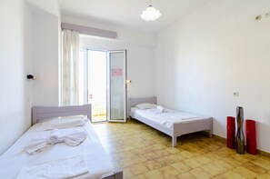 Una habitación con dos camas individuales, un ventanal corredero al exterior y suelo de baldosas.