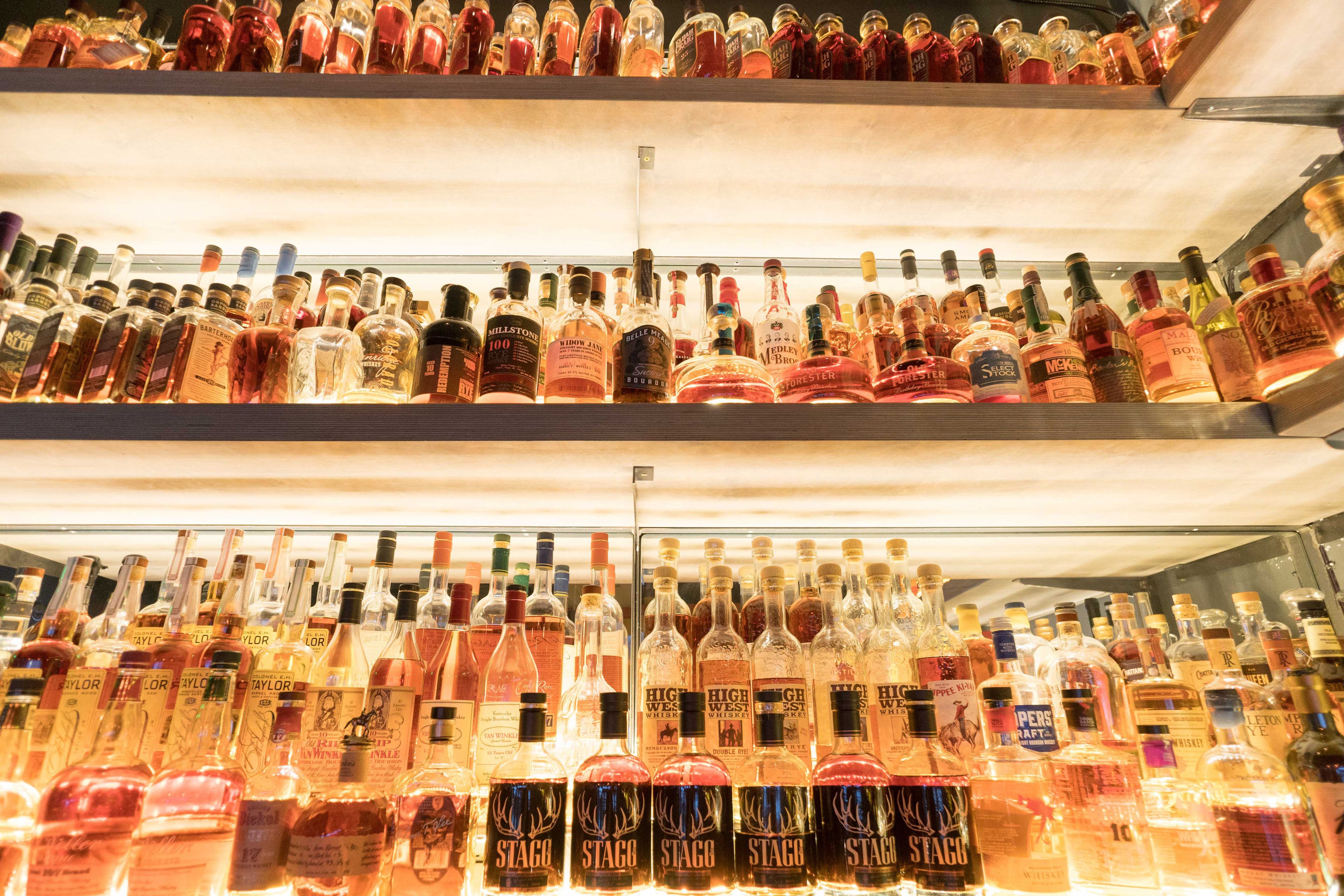 A display of various liquor bottles in a refrigerated case.