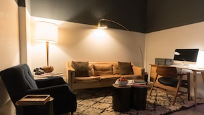 A cozy living room with a sofa, a coffee table, a desk with a computer, a lamp, and a chair. - The 404 Hotel (Nashville)