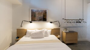 A neatly arranged hotel room with a bed, bedside lamps, a small wooden nightstand, a nightstand lamp, a framed picture on the wall, and a wooden dresser with a mirror. - The 404 Hotel (Nashville)