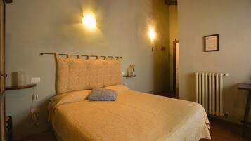 A bedroom with a bed, a nightstand, a wall-mounted light, a radiator, and a framed notice on the wall.