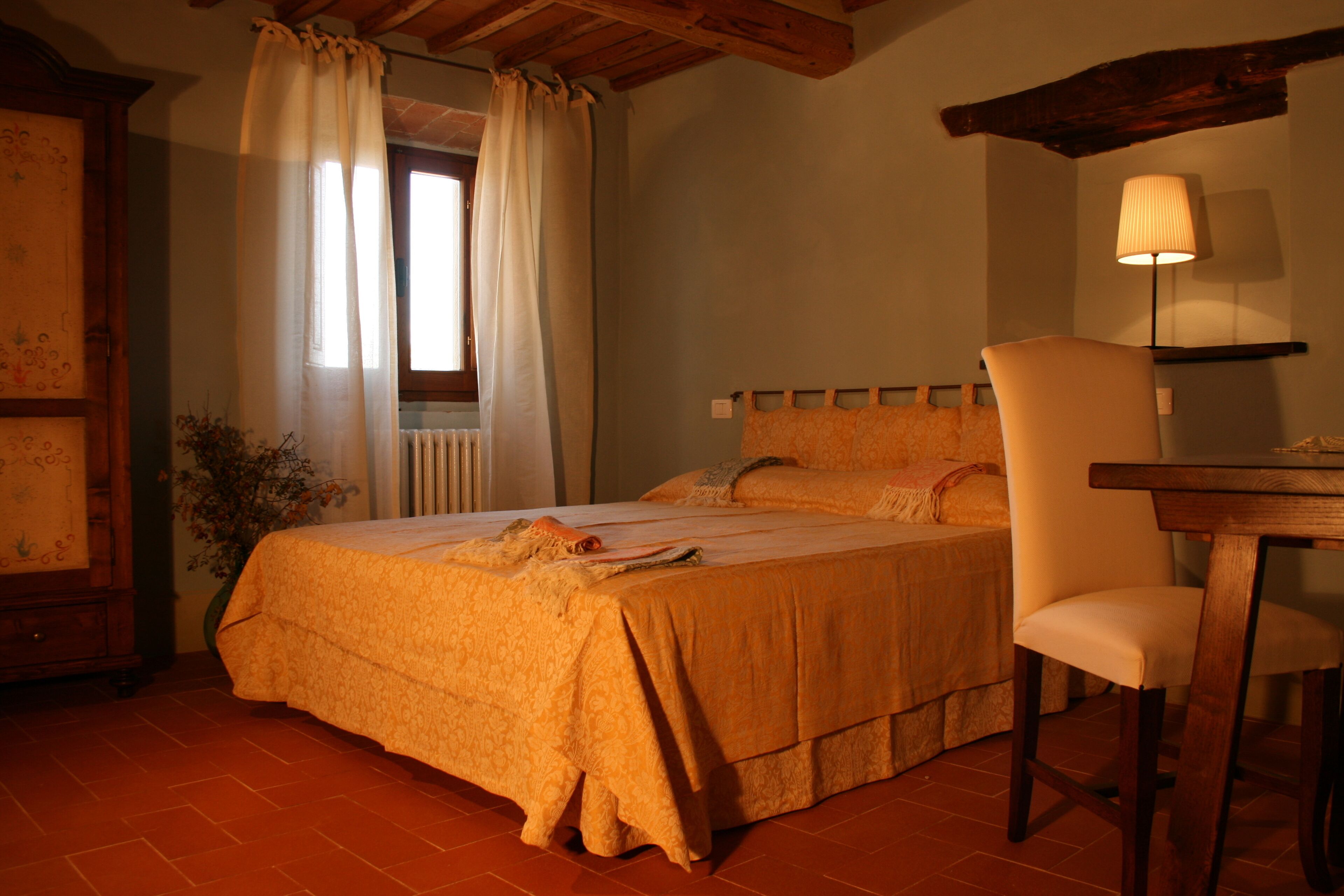 Un dormitorio con cama, una silla, una mesa y una lámpara.