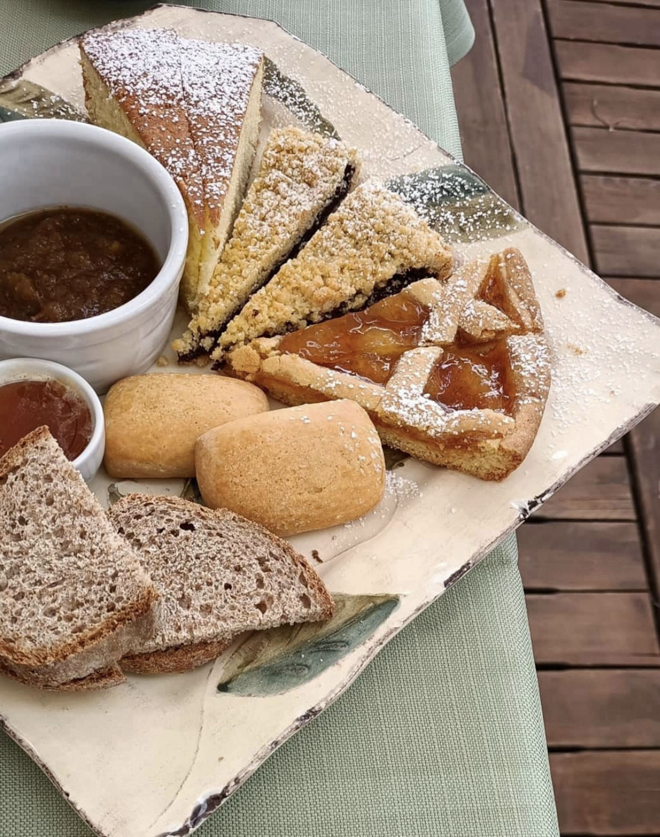 Ett fat med bitar av paj, kakor och bröd, samt små skålar med sylt och vaniljsås.