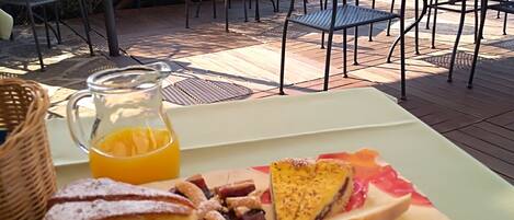 A breakfast table with various food items, including bread, pastries, and a jug of orange juice, set on an outdoor patio with chairs and tables.