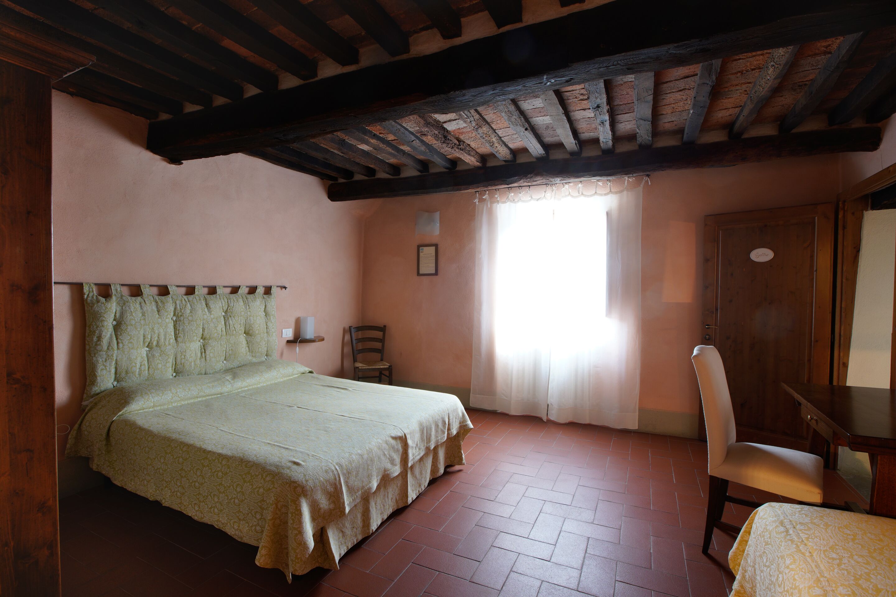 A bedroom with a bed, a chair, a desk, and a window with curtains.
