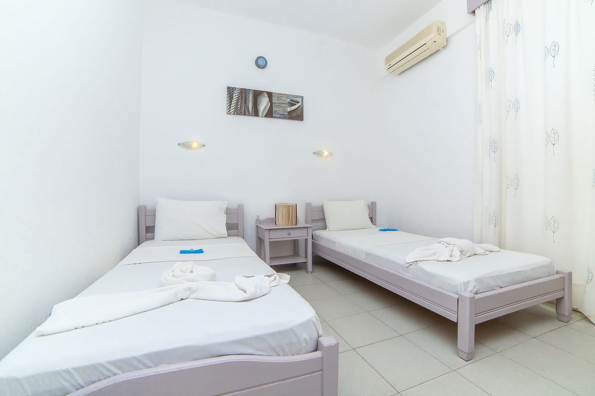 Ein Zimmer mit zwei Einzelbetten, einem Nachttisch, einer Wand-Klimaanlage und einer Deckenleuchte.