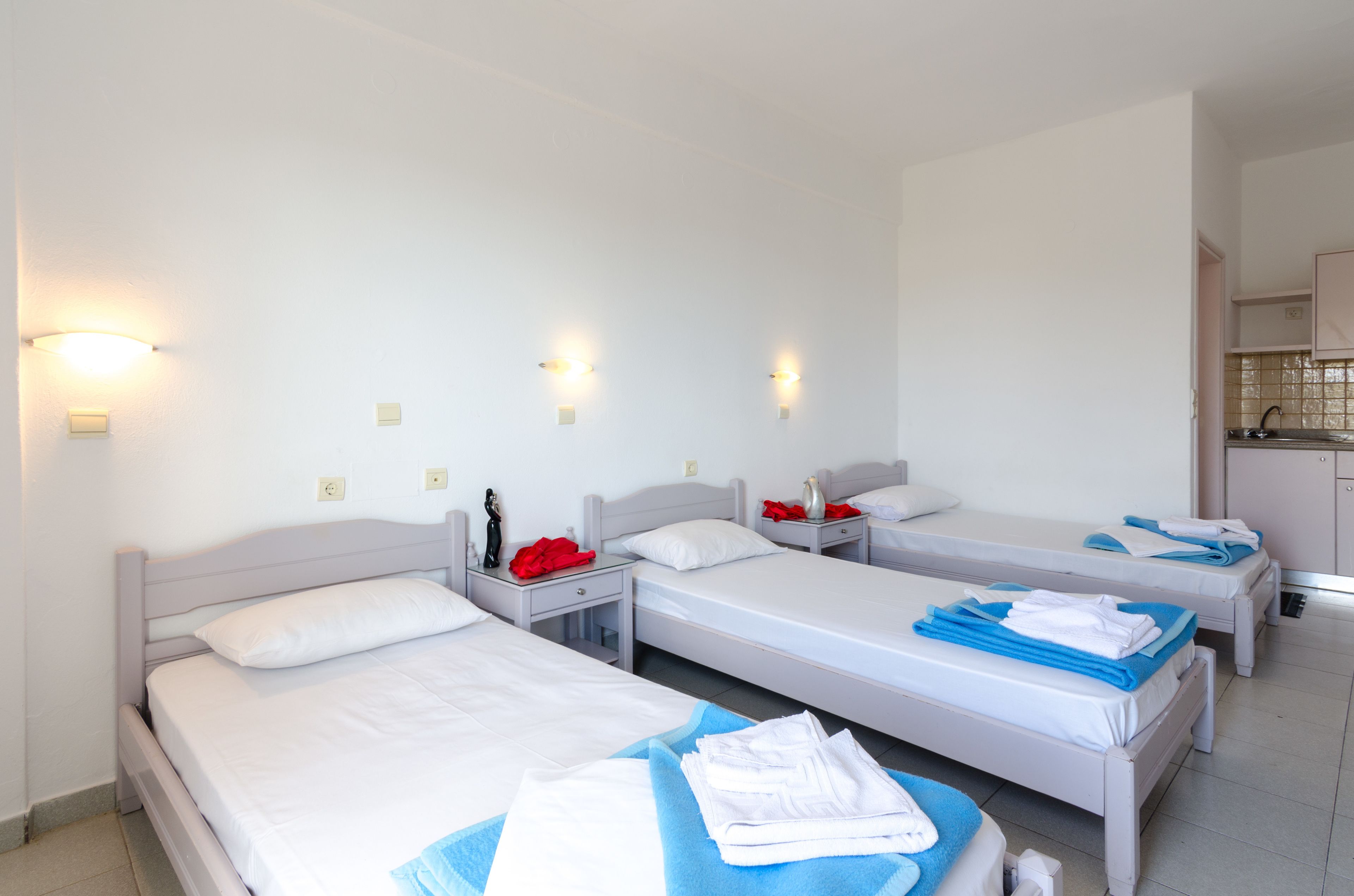 Una habitación de hotel con tres camas individuales, un escritorio pequeño y una kitchenette.