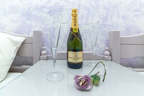 A bottle of Moët & Chandon champagne, two empty champagne flutes, and a purple artificial flower on a white table. - Stonewell (Hersonissos)