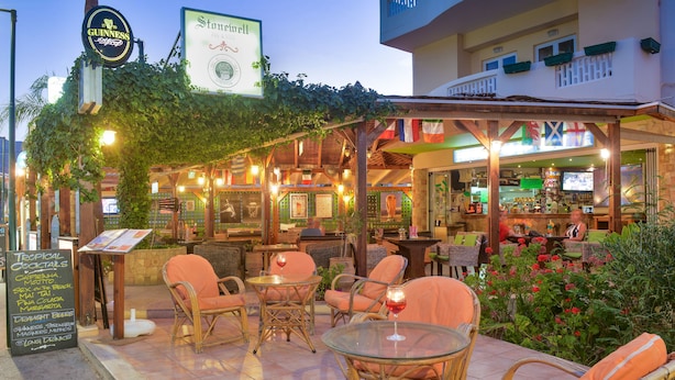 An outdoor bar area with wicker furniture and a menu board. - Stonewell (Hersonissos)