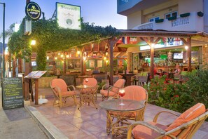 An outdoor bar area with wicker furniture and a menu board. - Stonewell (Hersonissos)