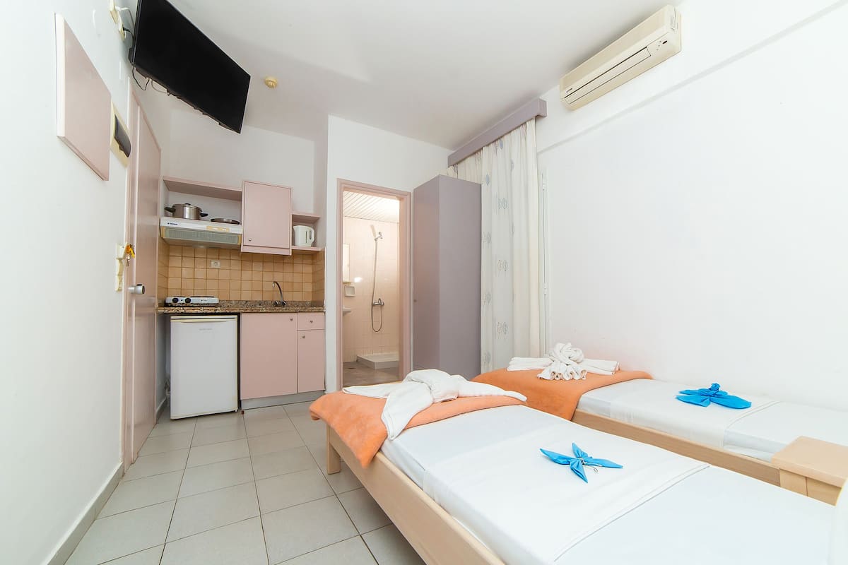 Ein kompaktes Hotelzimmer mit zwei Betten, einer Küchenzeile und einem Badezimmer mit Dusche.