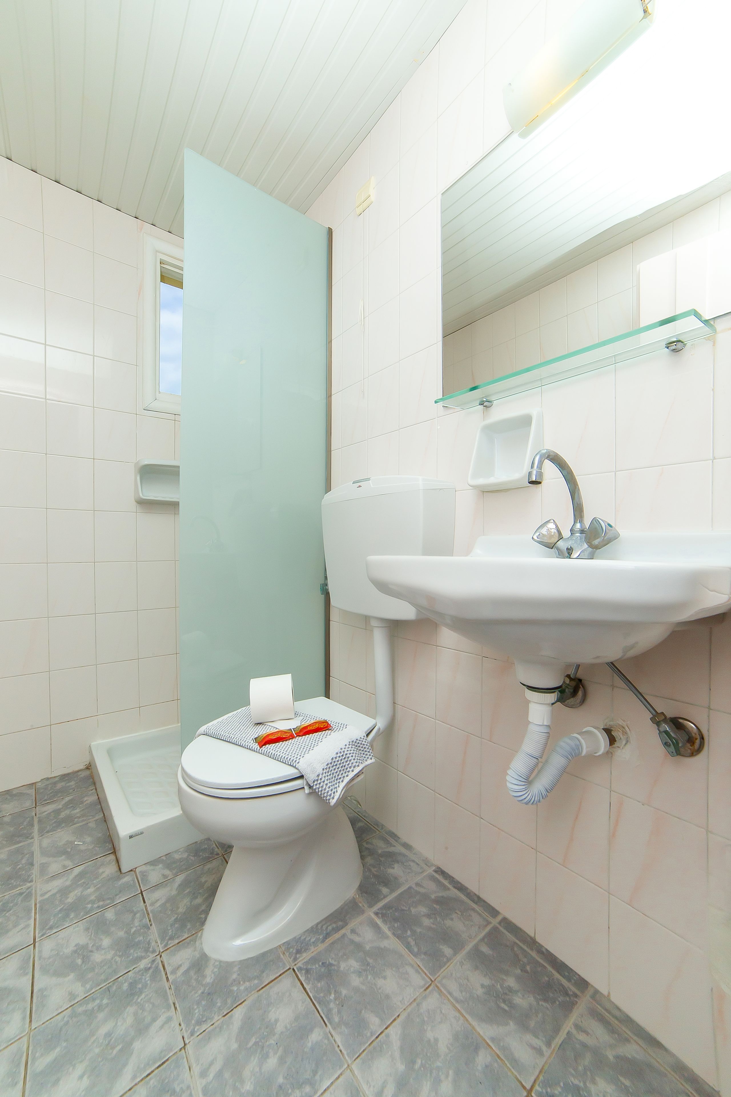 A bathroom with a white toilet, a glass shower enclosure, a white sink with a mirror above it, and a tiled floor.