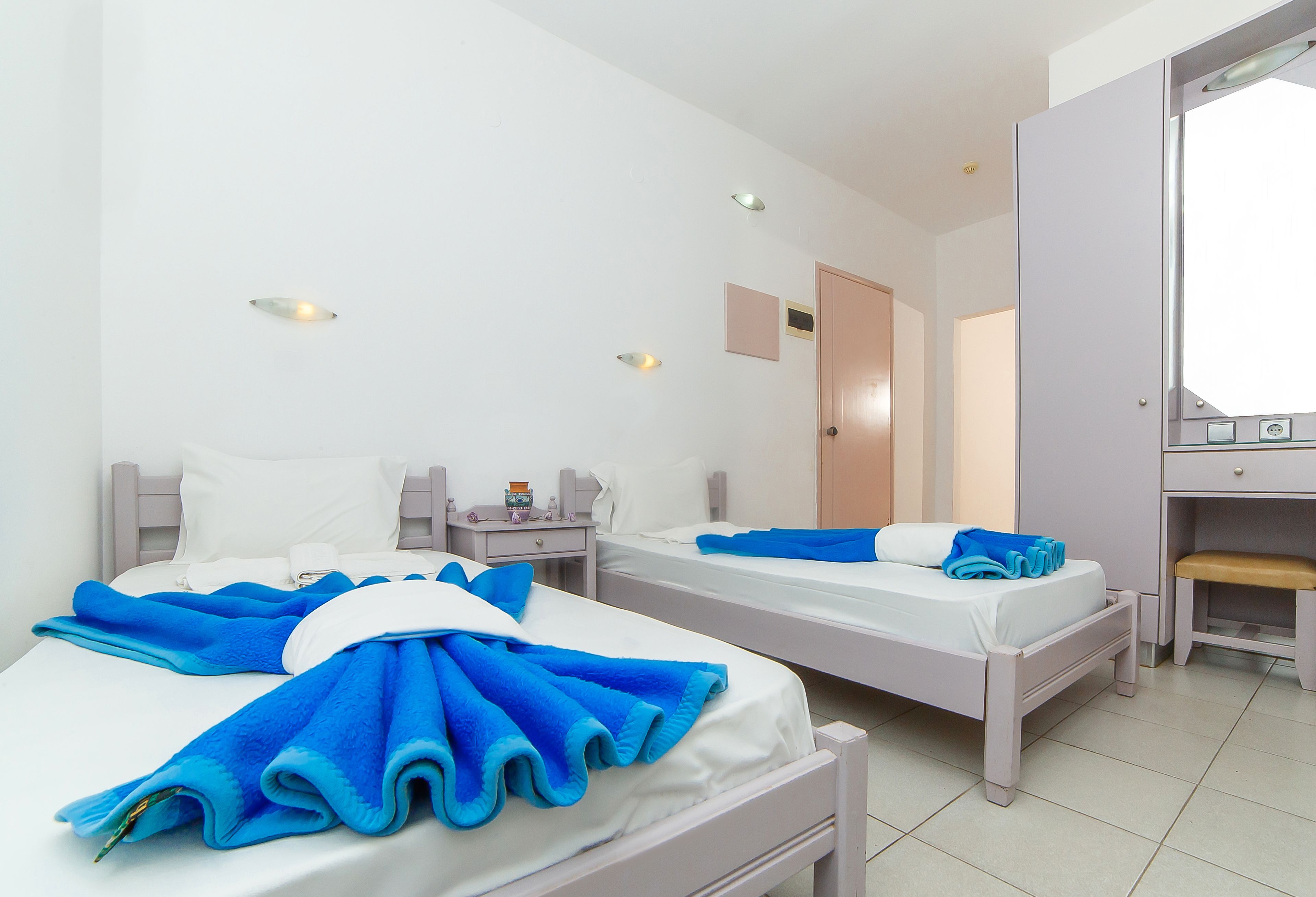 Une chambre d’hôtel avec deux lits, chacun équipé de serviettes bleues, de draps blancs et d’une table de chevet avec une lampe et un téléphone.