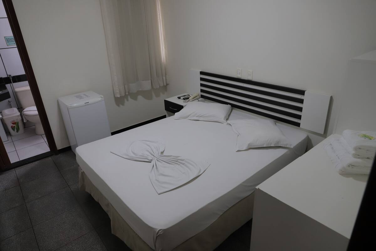 A hotel room with a bed, bedside table, and a small white cabinet.