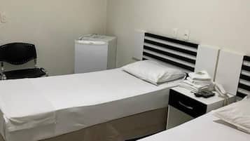 Hotellihuone, jossa on kaksi sänkyä, työpöytä, tuoli, pieni jääkaappi ja yöpöytä, jossa on lamppu.
