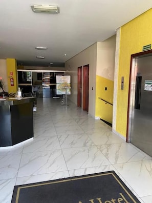 A hotel lobby with a reception desk, a refrigerator, and a door leading to another room. - Oft Neve's Hotel (Goiania)