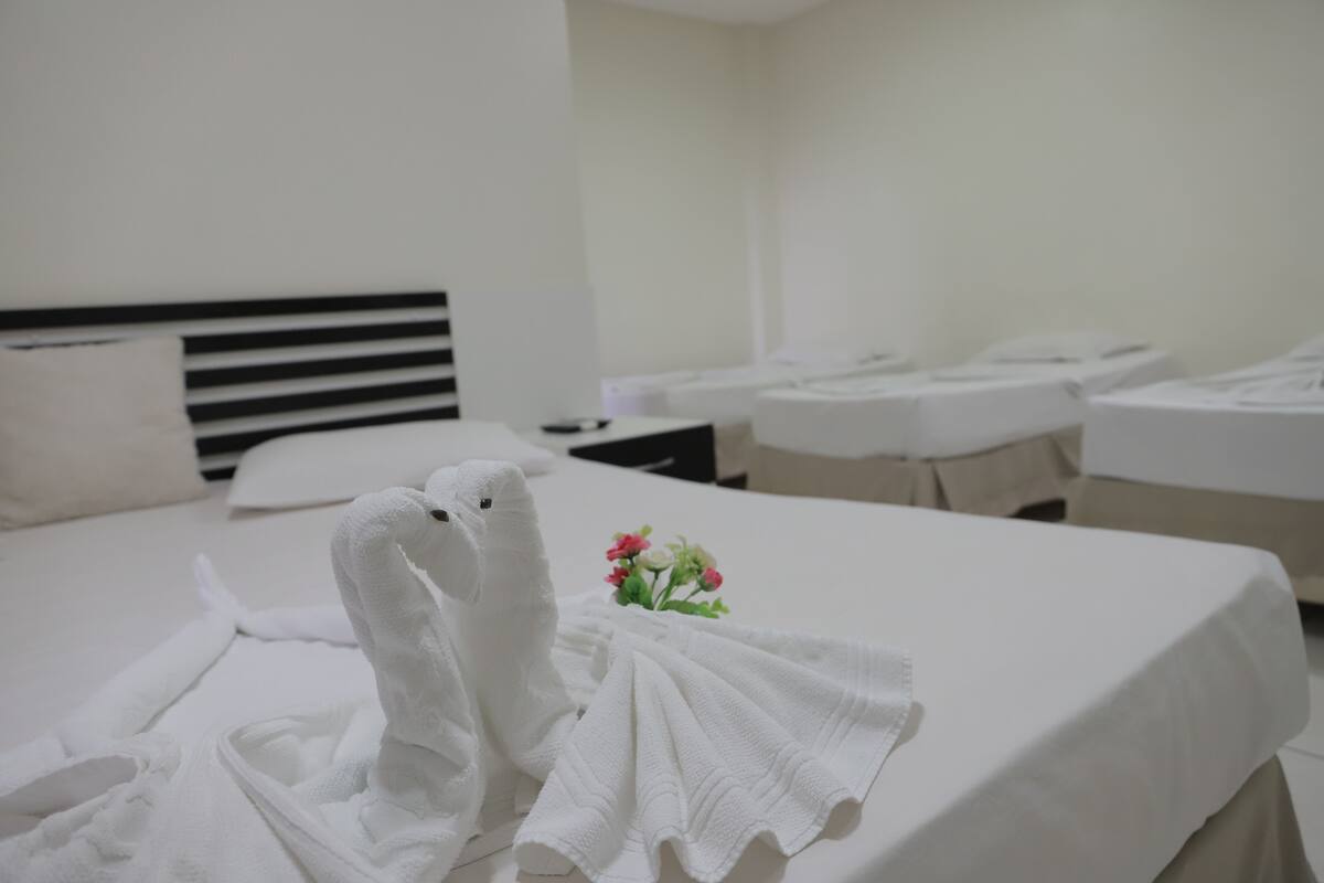 A hotel room with a neatly made bed, a bedside table with a lamp, and a small vase with flowers.