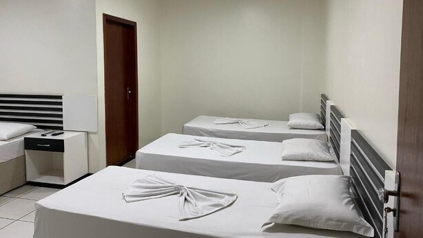 Una habitación de hotel con tres camas individuales, una mesita de noche con lámpara y un armario.