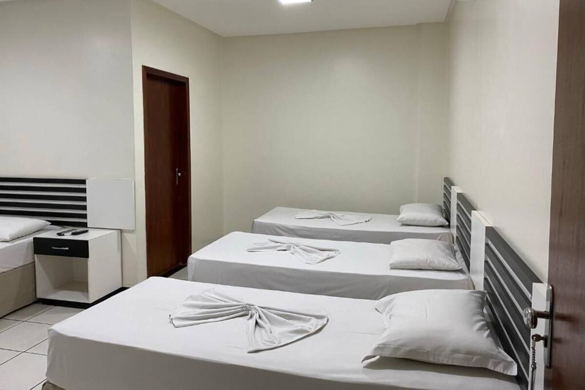 A hotel room with three single beds, a bedside table with a lamp, and a wardrobe.