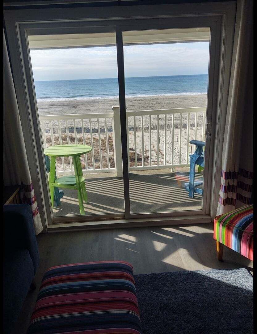 Une pièce dotée d’une grande porte-fenêtre coulissante donnant sur un balcon avec vue sur la plage et l’océan.