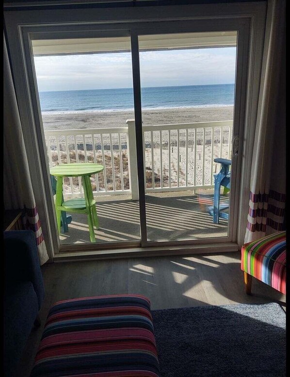 A room with a large sliding glass door leading to a balcony with a view of the beach and ocean. - Next 2 Paradise-203 2 Bedroom Condo by RedAwning (Supply)