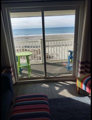 A room with a large sliding glass door leading to a balcony with a view of the beach and ocean.