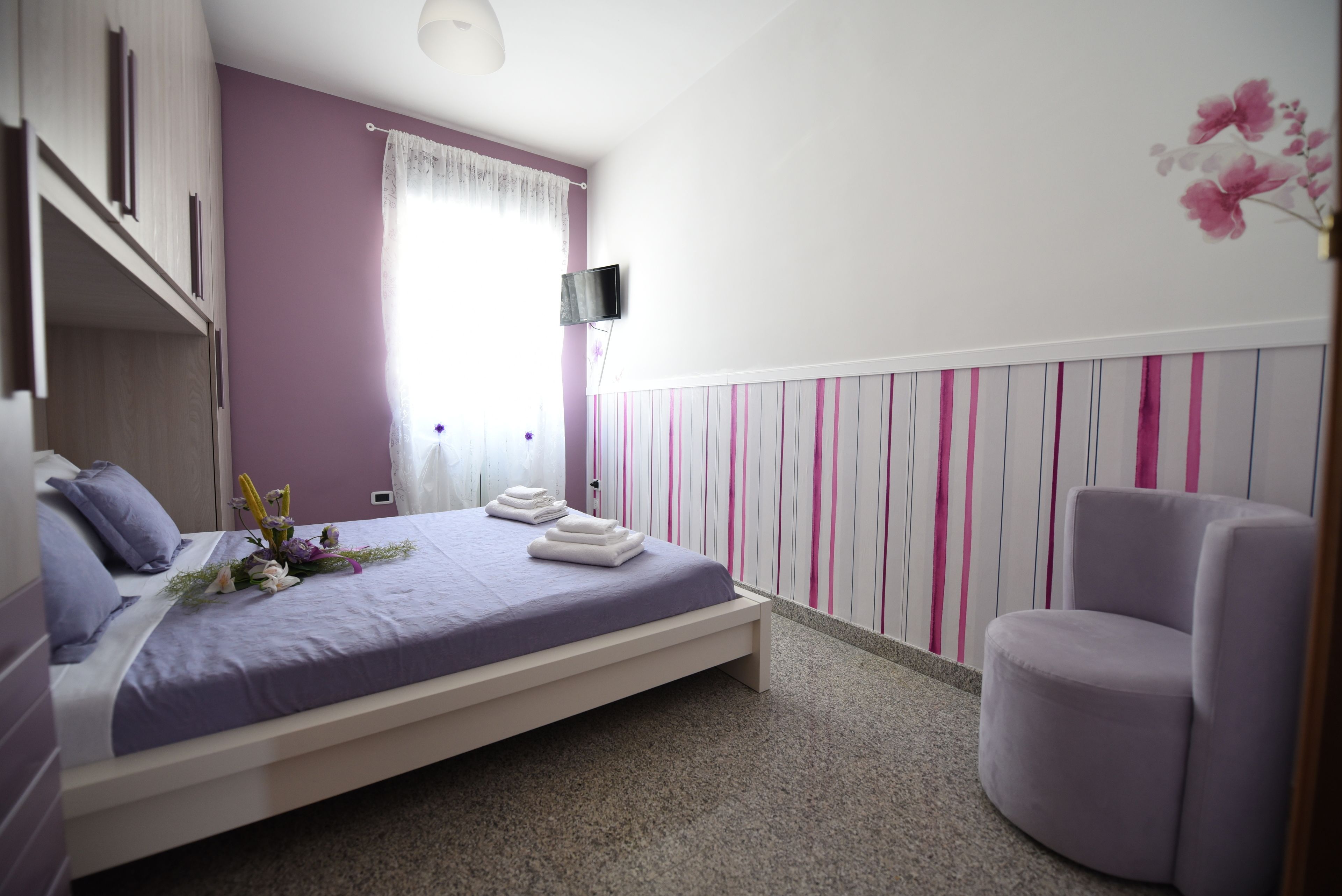 Una camera da letto con un letto, una sedia, un televisore e una parete a righe verticali.