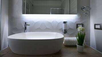 Ein modernes Badezimmer mit einem großen, ovalen Waschbecken, einem Handtuch, einer Topfpflanze und einem Spiegel.