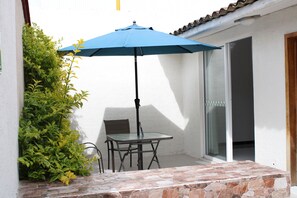 A patio with a table and chairs, a blue umbrella, and a stone-tiled floor.