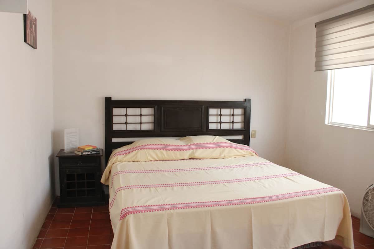 A bedroom with a bed, a nightstand, a window with blinds, and a wall-mounted picture.
