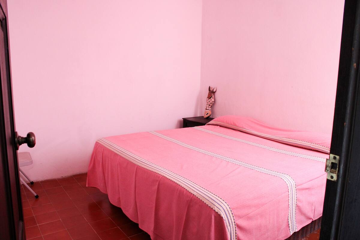 A small, pink-themed bedroom with a single bed, a nightstand, and a door.