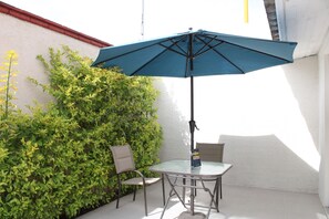 A small patio with a table and two chairs, an umbrella, and a hedge.