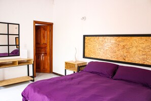 A bedroom with a bed, a wooden headboard, a desk with a mirror, and a door.