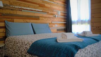 Una stanza con parete in listelli di legno, un letto con copriletto a fantasia, due cuscini, una coperta azzurra e un asciugamano arrotolato sul letto.
