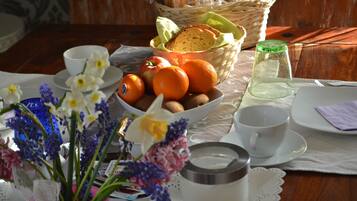 Un tavolo con una ciotola di arance, un cesto di pane, un bicchiere d'acqua e un vaso di fiori.