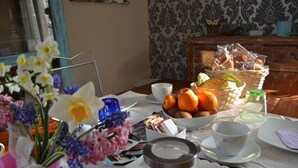 A dining table with a variety of food items, a vase with flowers, and a wicker basket with bread. - B&B Cappuccini (Schio)
