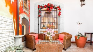 A wicker sofa with red cushions, a glass-top coffee table, and a potted plant. - Capital O El Nito Posada (Oaxaca)