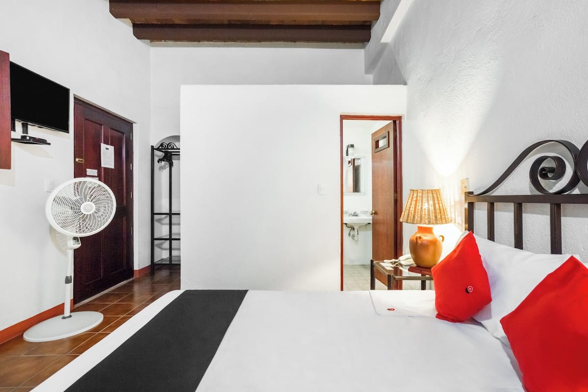 Habitación de hotel con cama, ventilador, lámpara y vistas al baño.