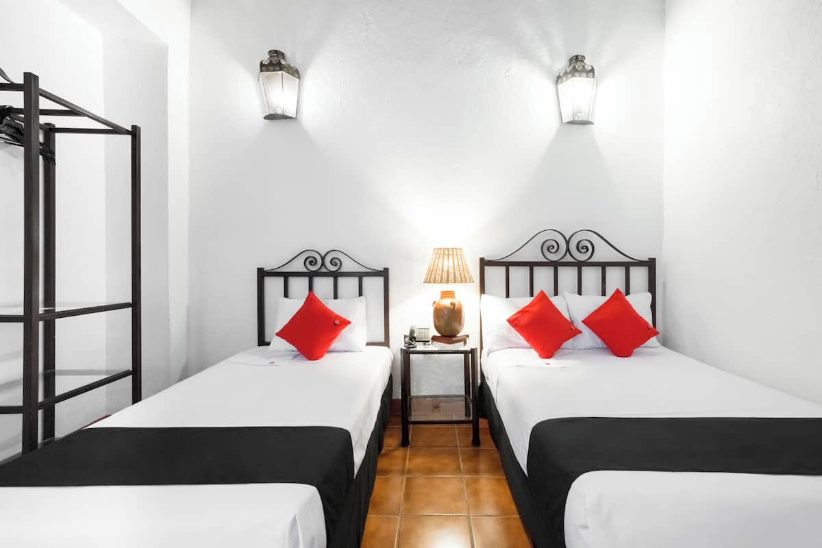 Habitación de hotel con dos camas, una mesita con lámpara y ventana con vistas al exterior.