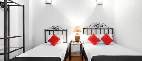 A hotel room with two beds, a small table with a lamp, and a window with a view of the outside.
