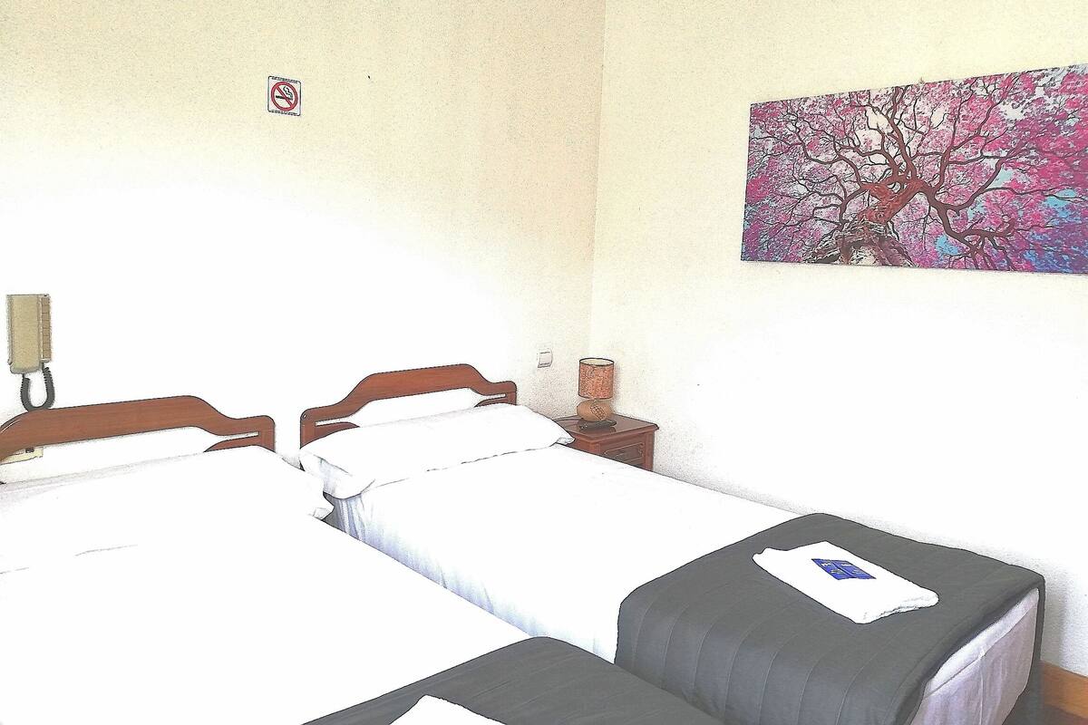 A room with two beds, a nightstand with a lamp, and a wall painting.