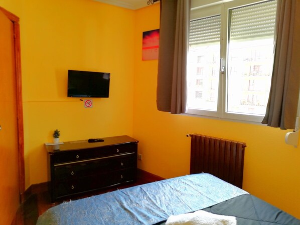 A bedroom with a bed, a dresser, a television, and a window with curtains. - Pensión Txoko-Maitea (Urnieta)