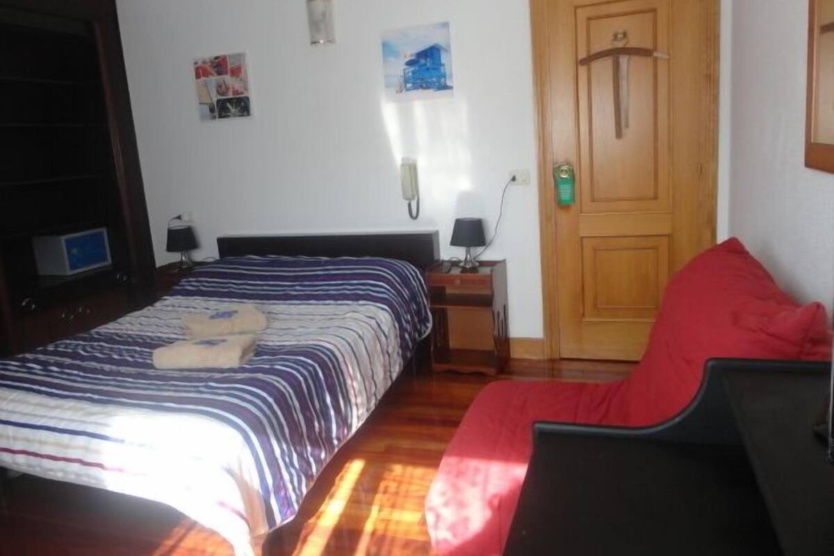 A bedroom with a bed, bedside tables, a desk, and a door.